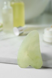 Jade gua sha tool and toiletries on white table, closeup