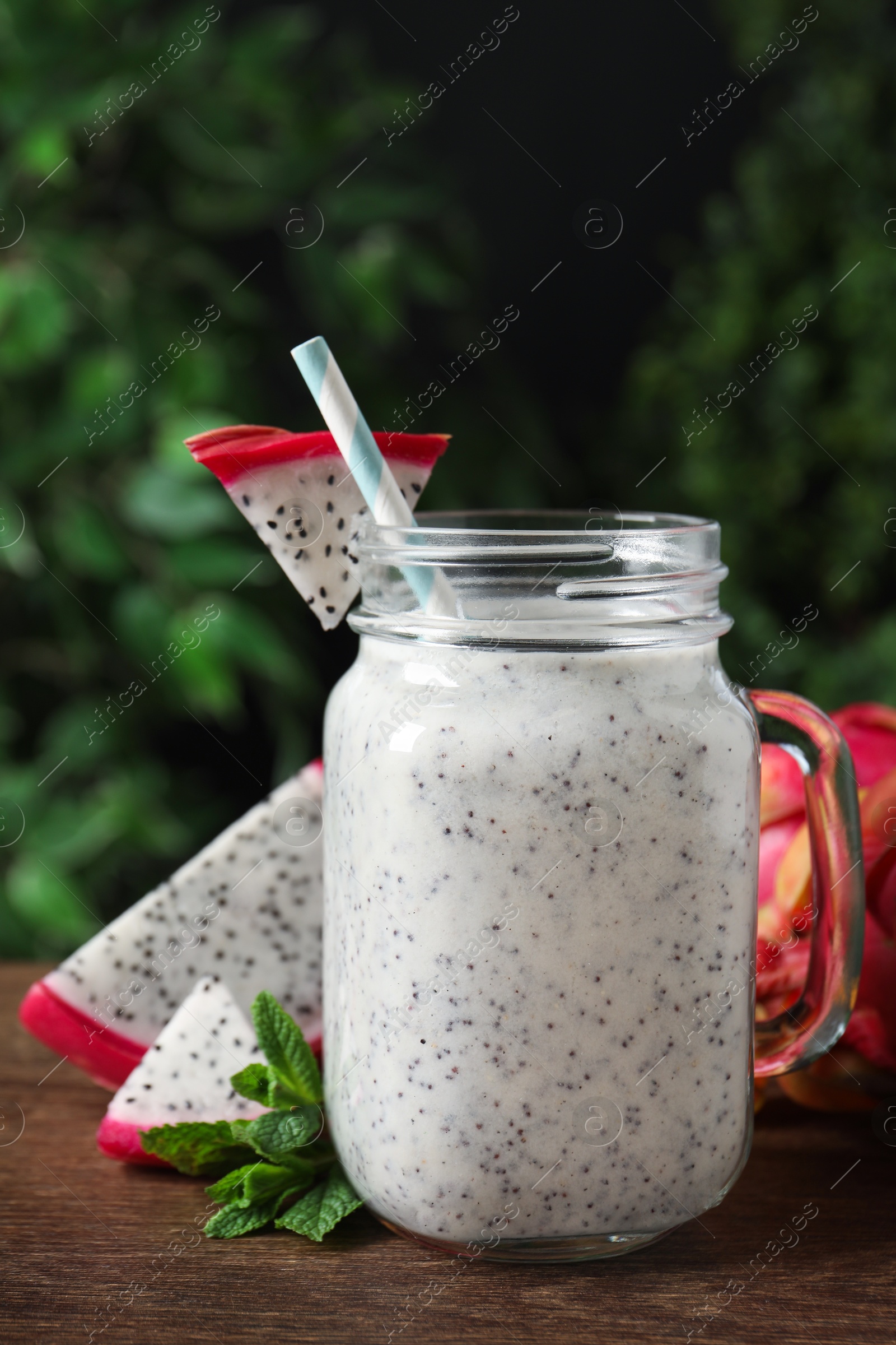 Photo of Delicious pitahaya smoothie in mason jar and fresh fruits on wooden table