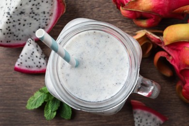 Photo of Delicious pitahaya smoothie in mason jar and fresh fruits on wooden table, flat lay