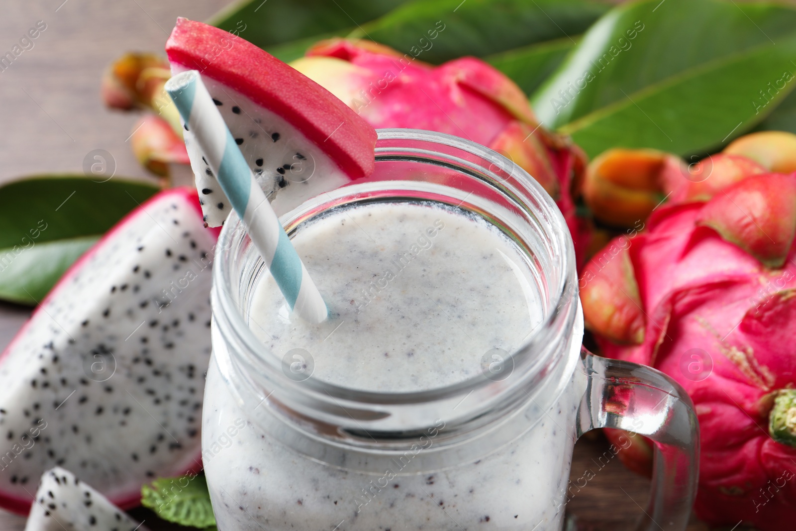 Photo of Delicious pitahaya smoothie in mason jar and fresh fruits on table, closeup