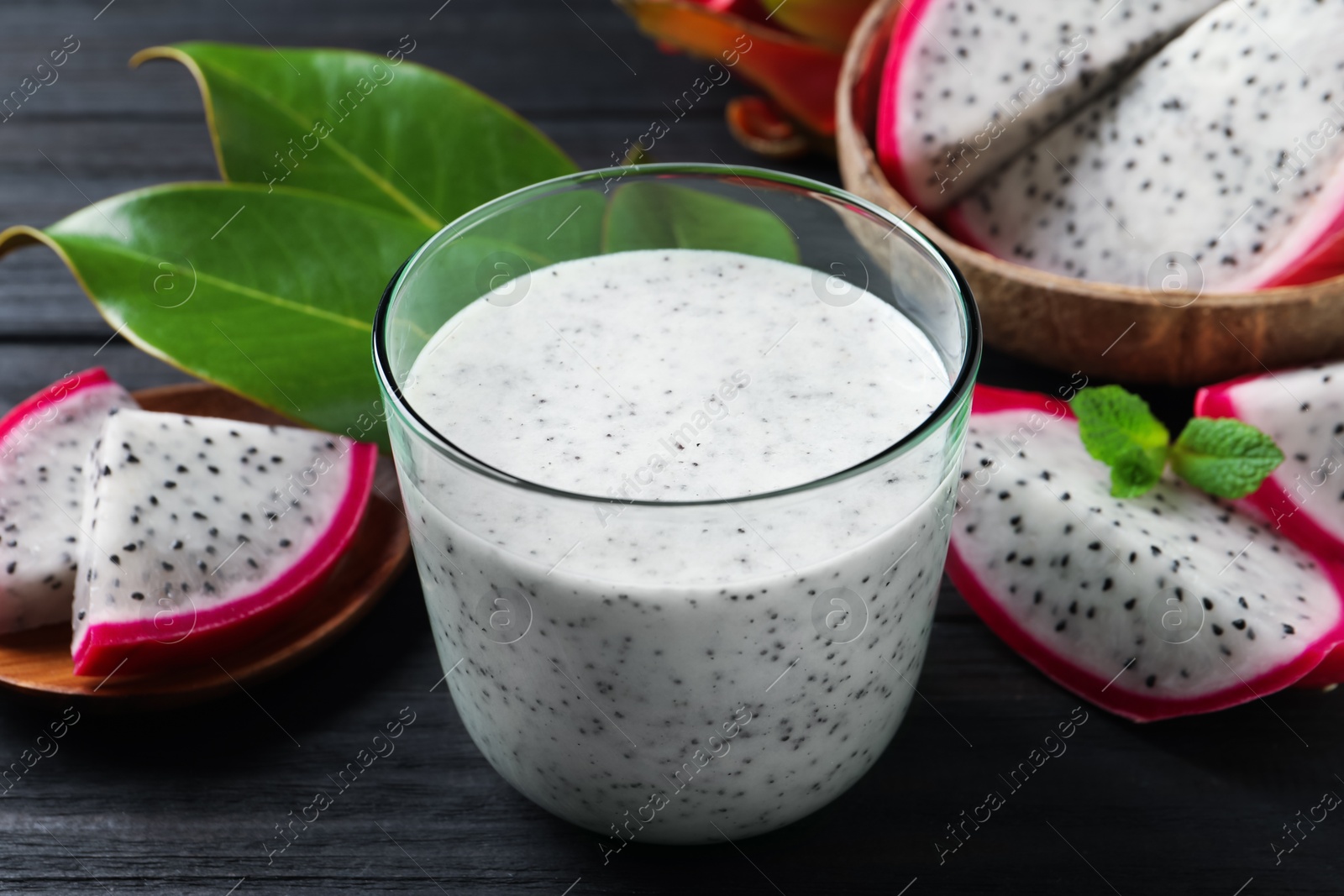 Photo of Delicious pitahaya smoothie and fresh fruits on black wooden table, closeup