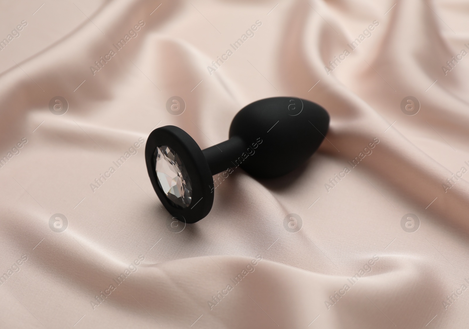 Photo of Black anal plug on beige silky fabric. Sex toy