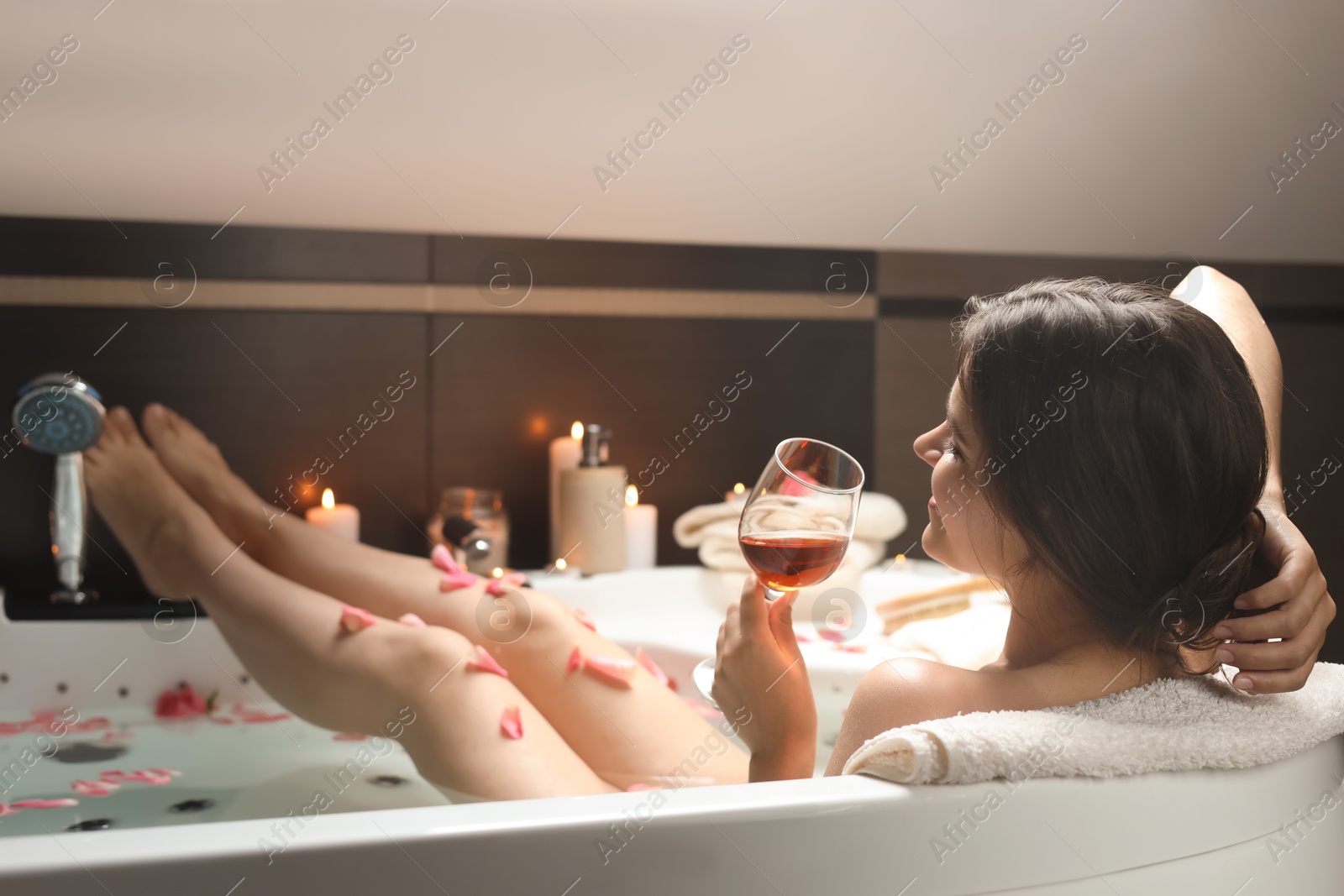 Photo of Woman holding glass of wine while taking bath with rose petals. Romantic atmosphere