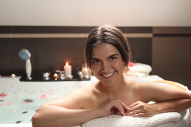 Photo of Happy beautiful woman taking bath with flower petals indoors. Romantic atmosphere