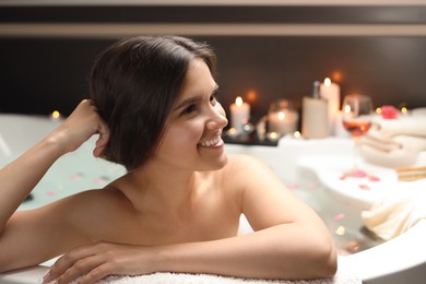 Photo of Happy beautiful woman taking bath with flower petals indoors. Romantic atmosphere
