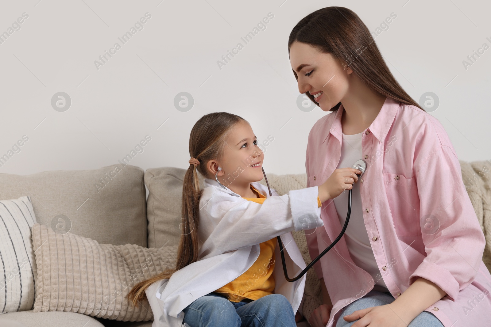 Photo of Little girl playing doctor with her mother at home. Space for text