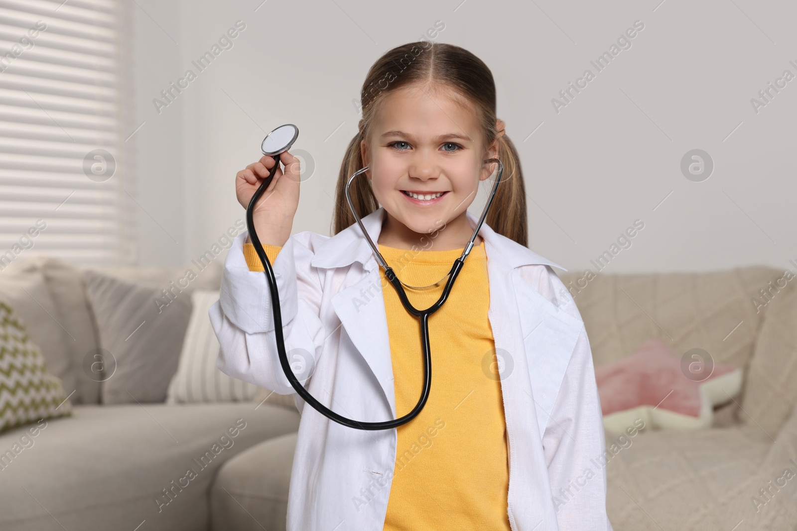 Photo of Little girl in medical uniform with stethoscope at home