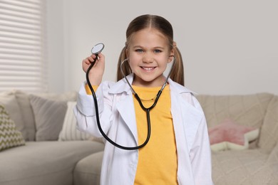 Photo of Little girl in medical uniform with stethoscope at home