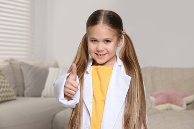 Photo of Little girl in medical uniform showing thumb up at home
