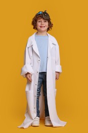 Photo of Little boy in medical uniform with head mirror on yellow background