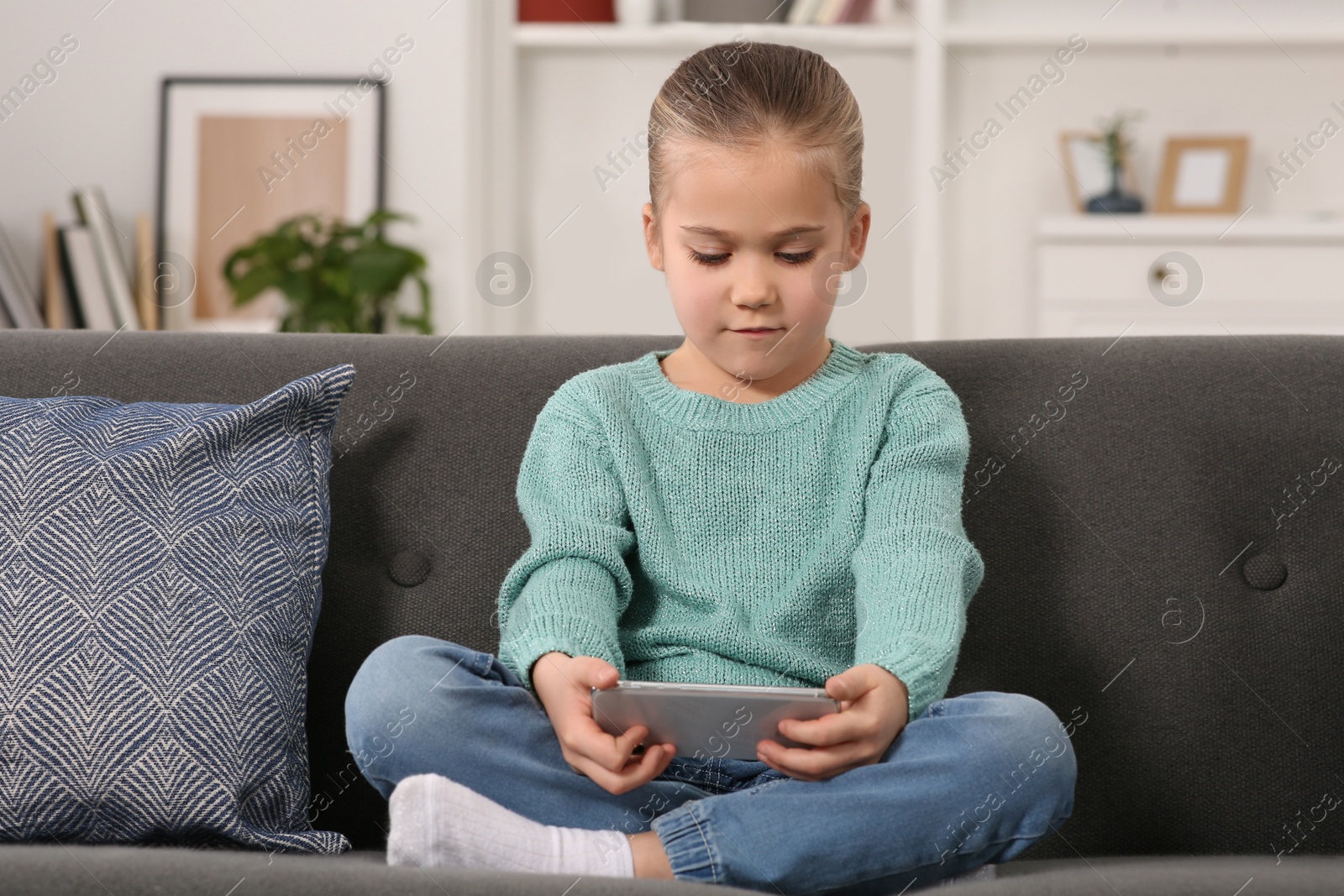 Photo of Little girl using smartphone on sofa at home. Internet addiction