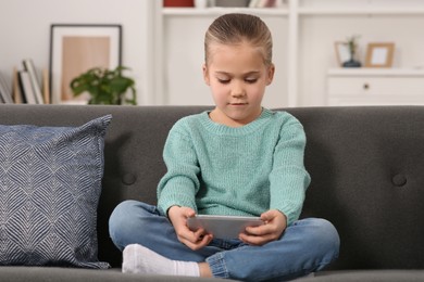 Photo of Little girl using smartphone on sofa at home. Internet addiction