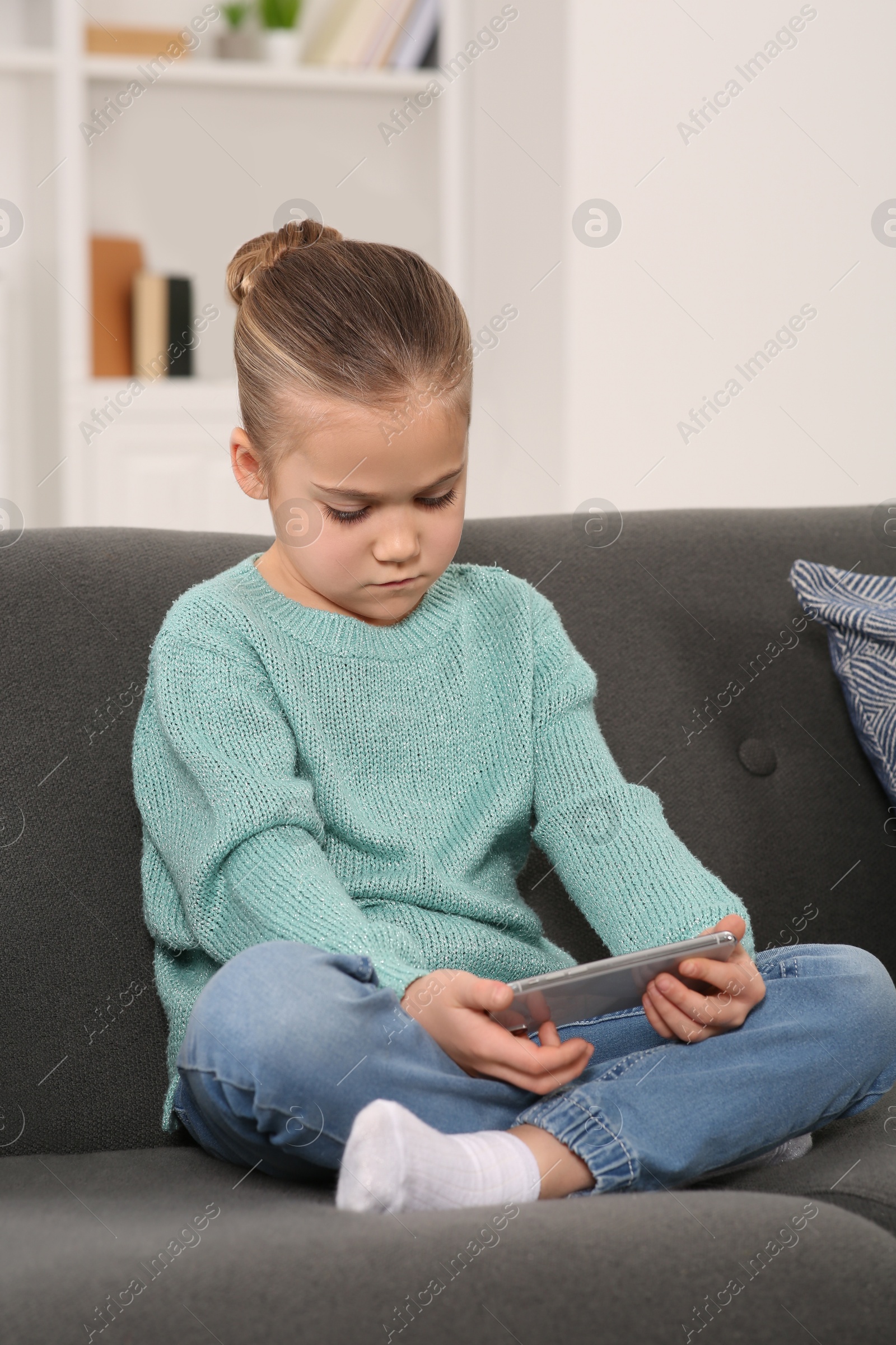 Photo of Little girl using smartphone on sofa at home. Internet addiction