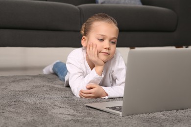 Photo of Little girl using laptop on floor at home. Internet addiction