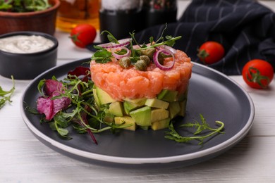 Tasty salmon tartare with avocado and greens on white wooden table, closeup