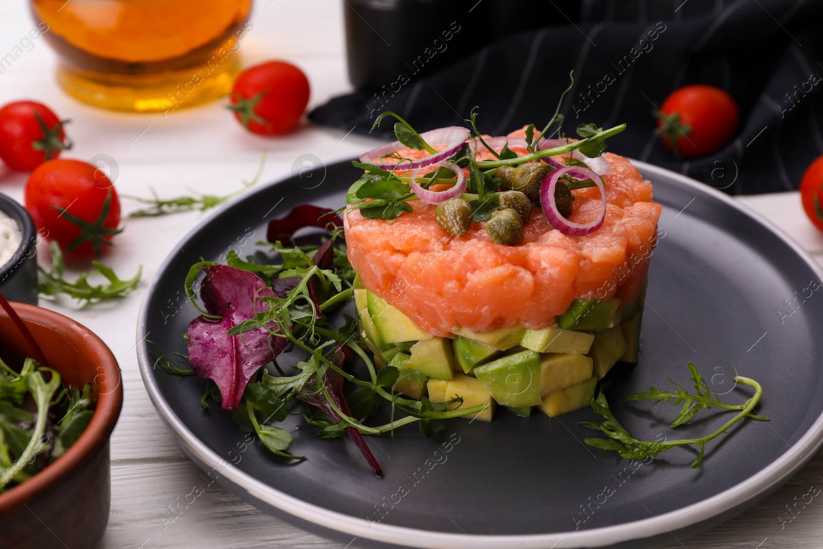 Photo of Tasty salmon tartare with avocado and greens on white wooden table, closeup