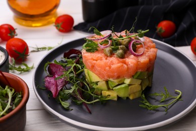 Photo of Tasty salmon tartare with avocado and greens on white wooden table, closeup