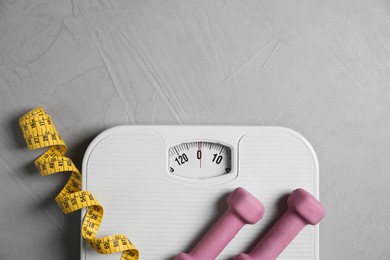 Photo of Bathroom scale, measuring tape and dumbbells on grey textured background, flat lay. Space for text