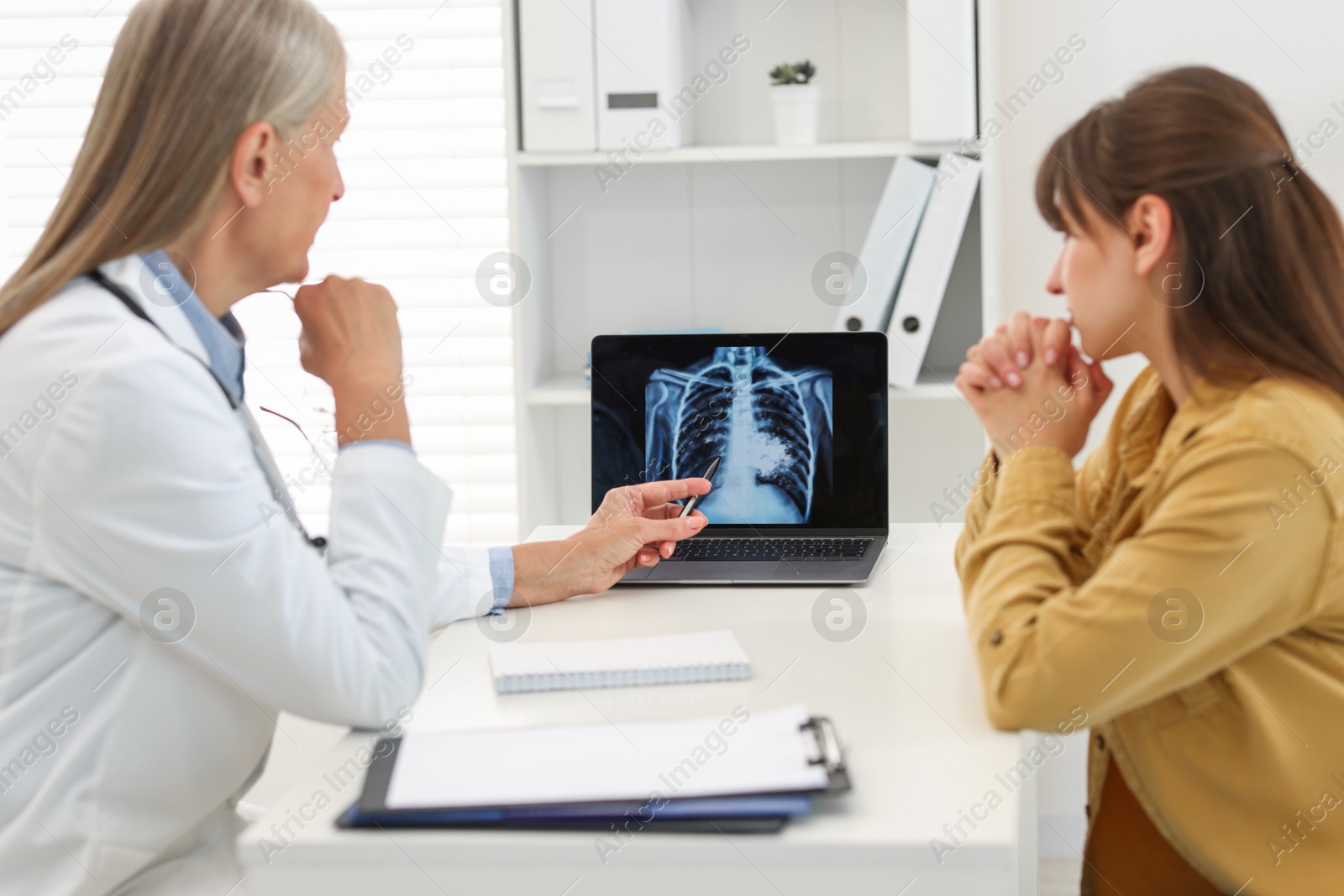 Photo of Lung cancer. Doctor showing chest x-ray on laptop to her patient in clinic