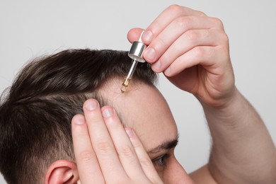 Photo of Baldness concept. Man dripping serum onto his hair on light grey background, closeup