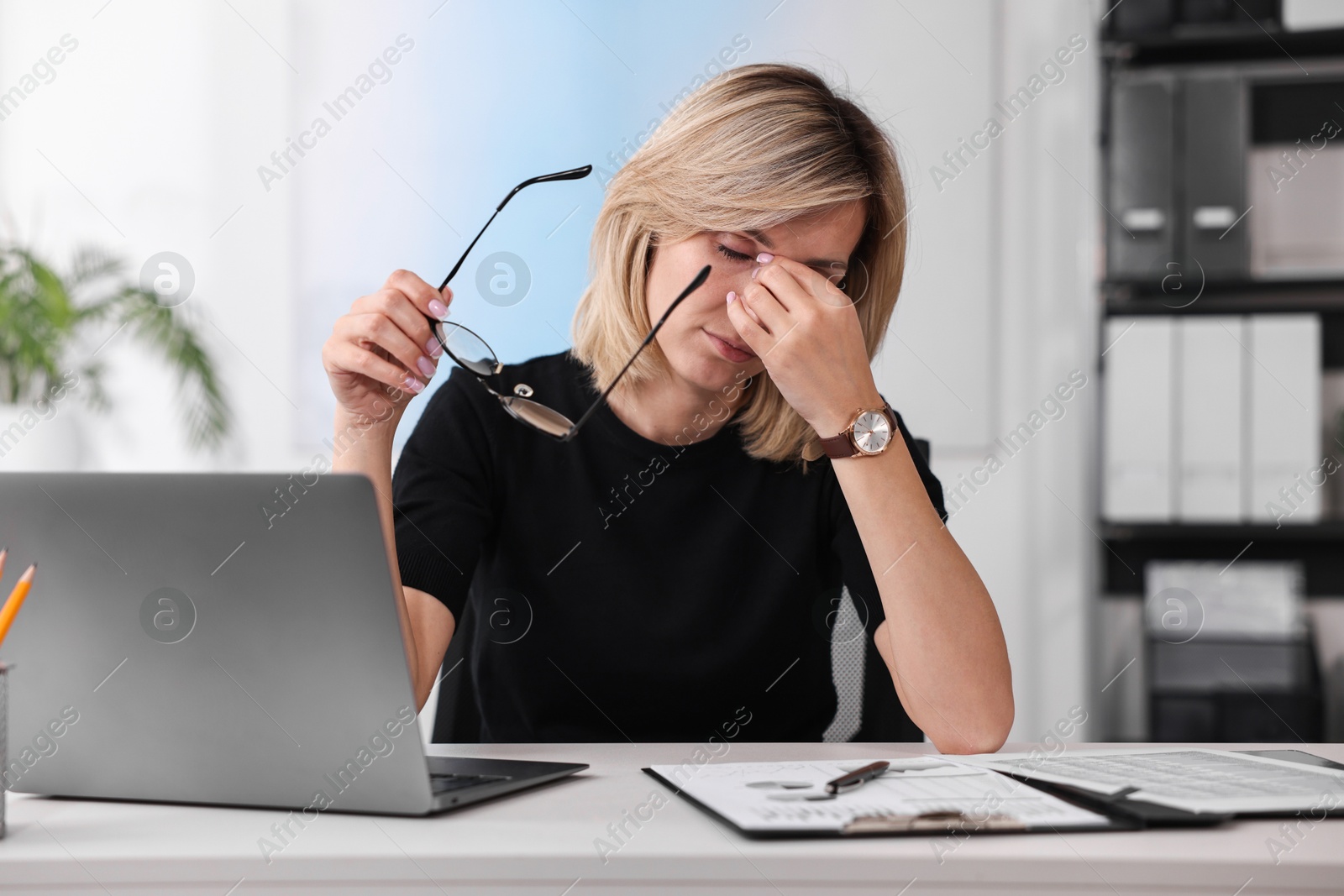 Photo of Overwhelmed woman with glasses sitting at table in office