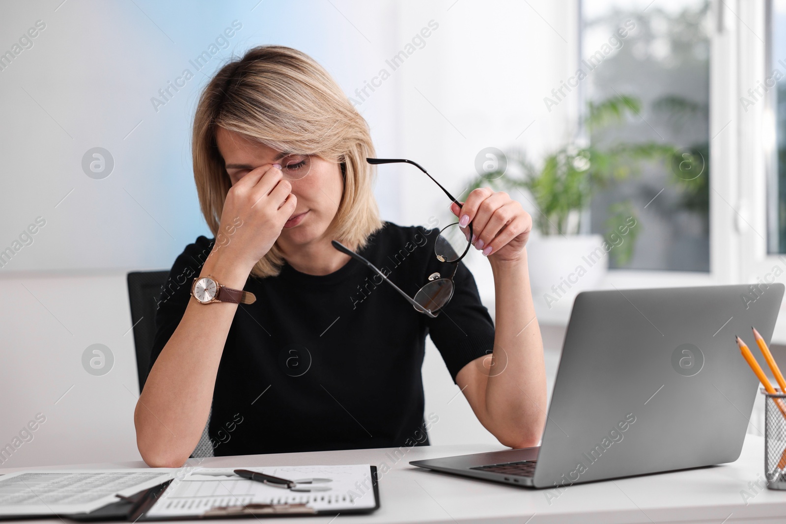 Photo of Overwhelmed woman with glasses sitting at table in office