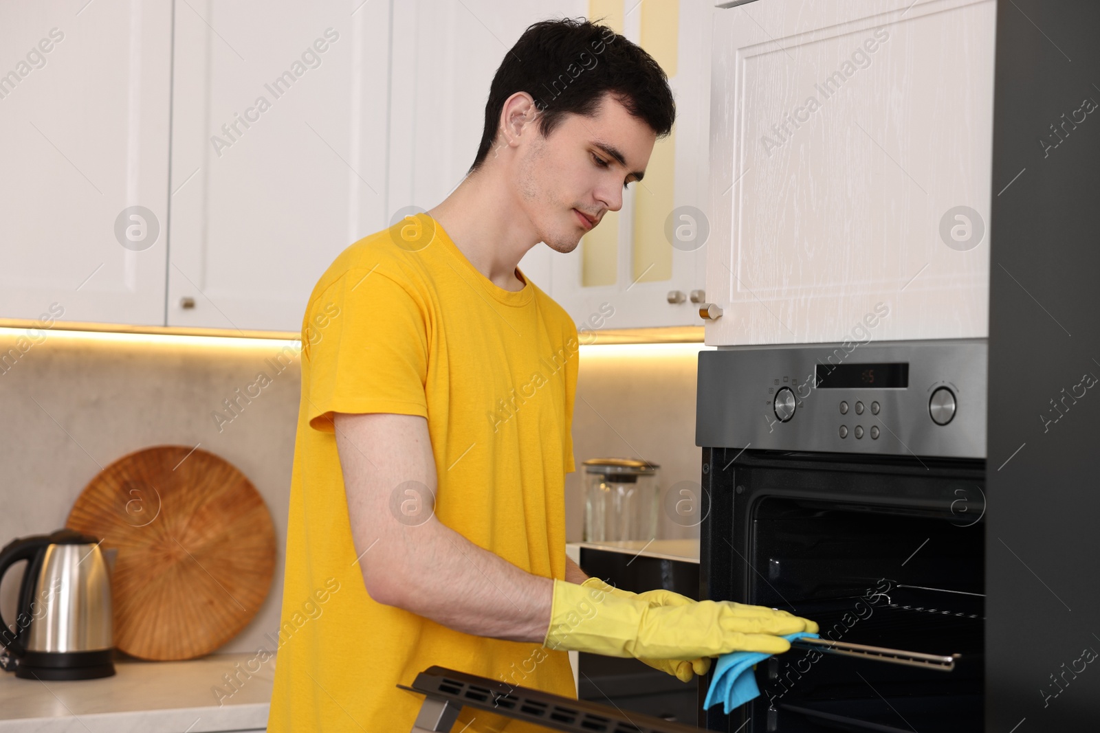 Photo of Professional janitor wearing uniform cleaning electric oven in kitchen