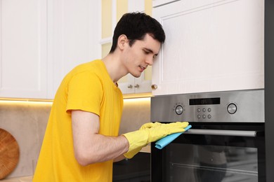 Photo of Professional janitor wearing uniform cleaning electric oven in kitchen