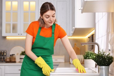 Photo of Professional janitor wearing uniform cleaning sink in kitchen