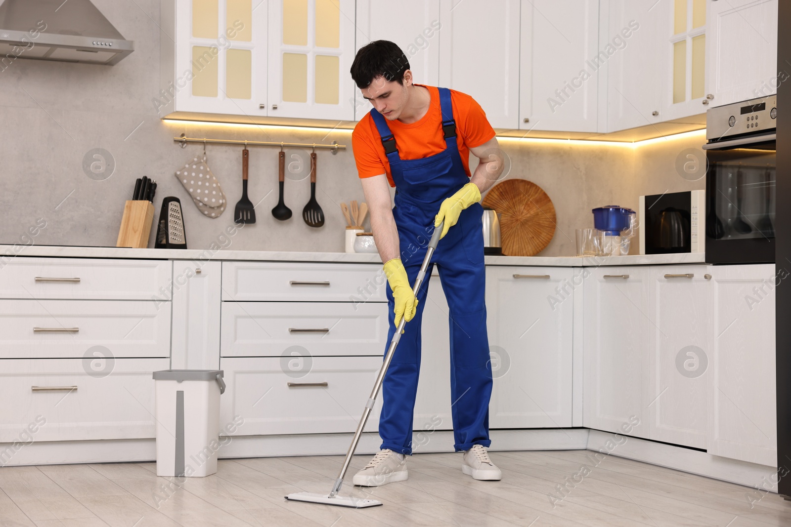 Photo of Cleaning service worker washing floor with mop in kitchen