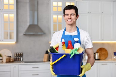 Photo of Cleaning service worker holding bucket with supplies in kitchen. Space for text