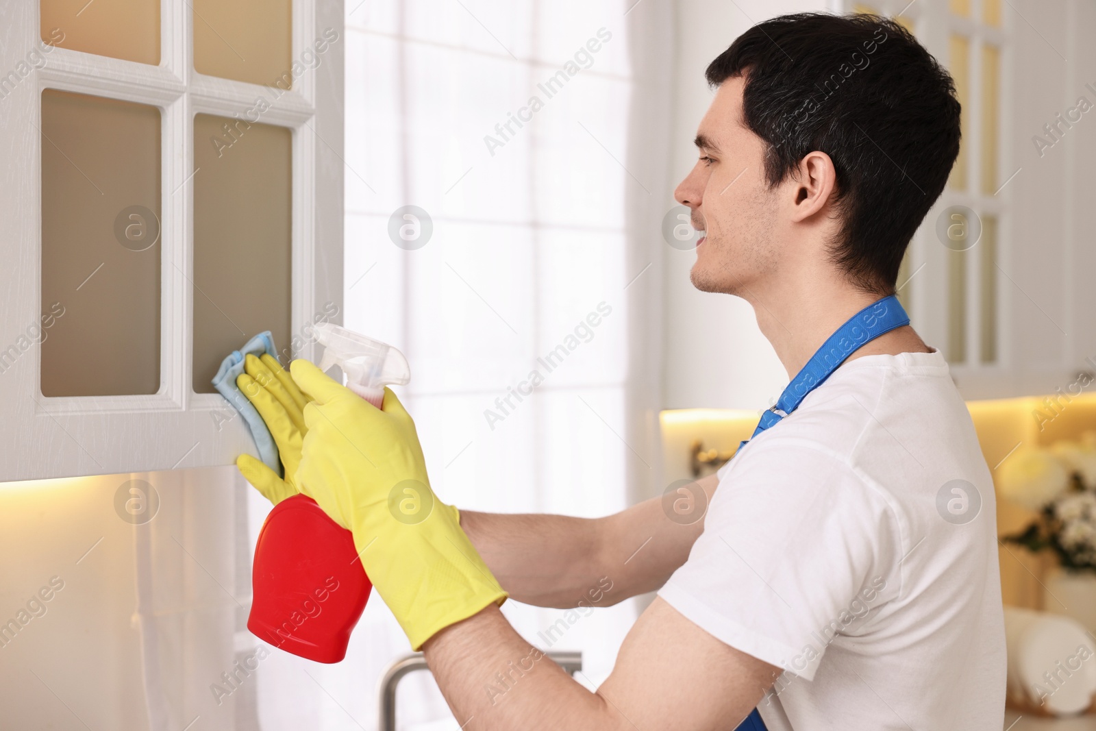 Photo of Professional janitor wearing uniform cleaning cabinet in kitchen