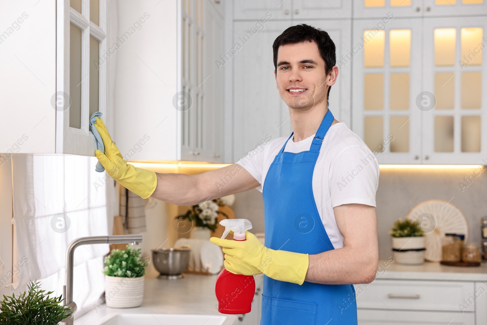 Photo of Professional janitor wearing uniform cleaning cabinet in kitchen