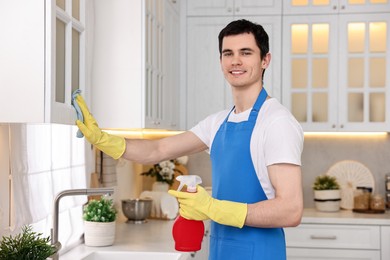 Photo of Professional janitor wearing uniform cleaning cabinet in kitchen