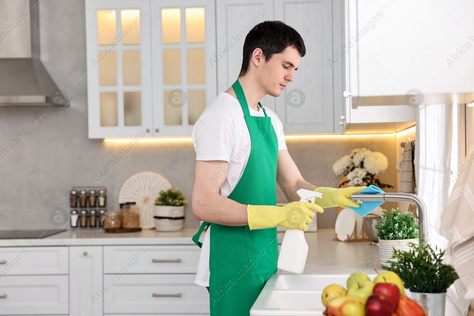 Photo of Professional janitor cleaning tap with rag and detergent in kitchen