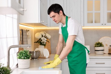 Photo of Professional janitor wearing uniform cleaning countertop in kitchen