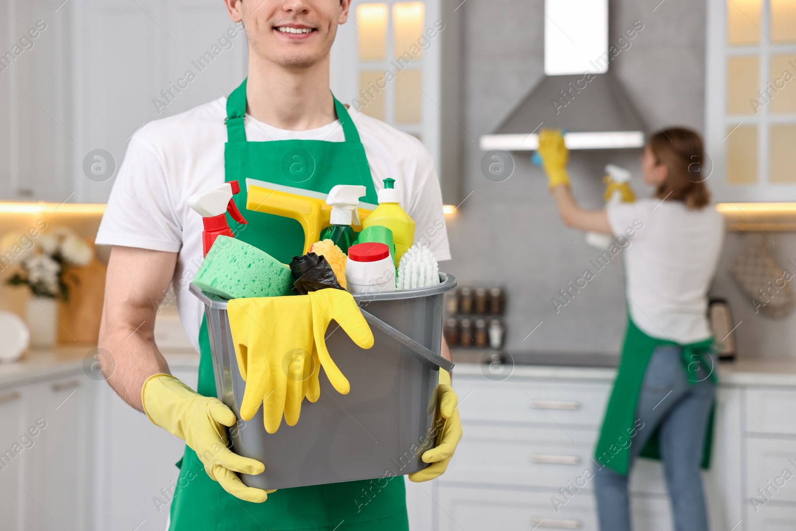 Photo of Cleaning service worker holding bucket with supplies in kitchen, closeup