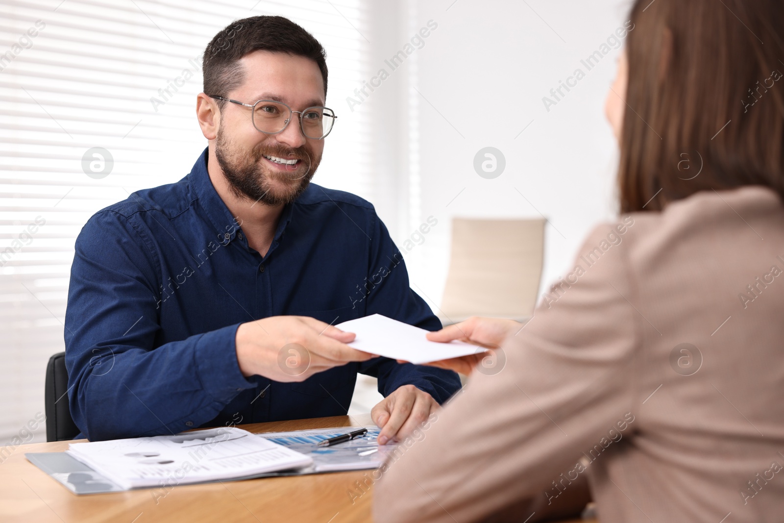 Photo of Boss giving salary in paper envelope to employee indoors