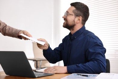 Photo of Boss giving salary in paper envelope to employee indoors