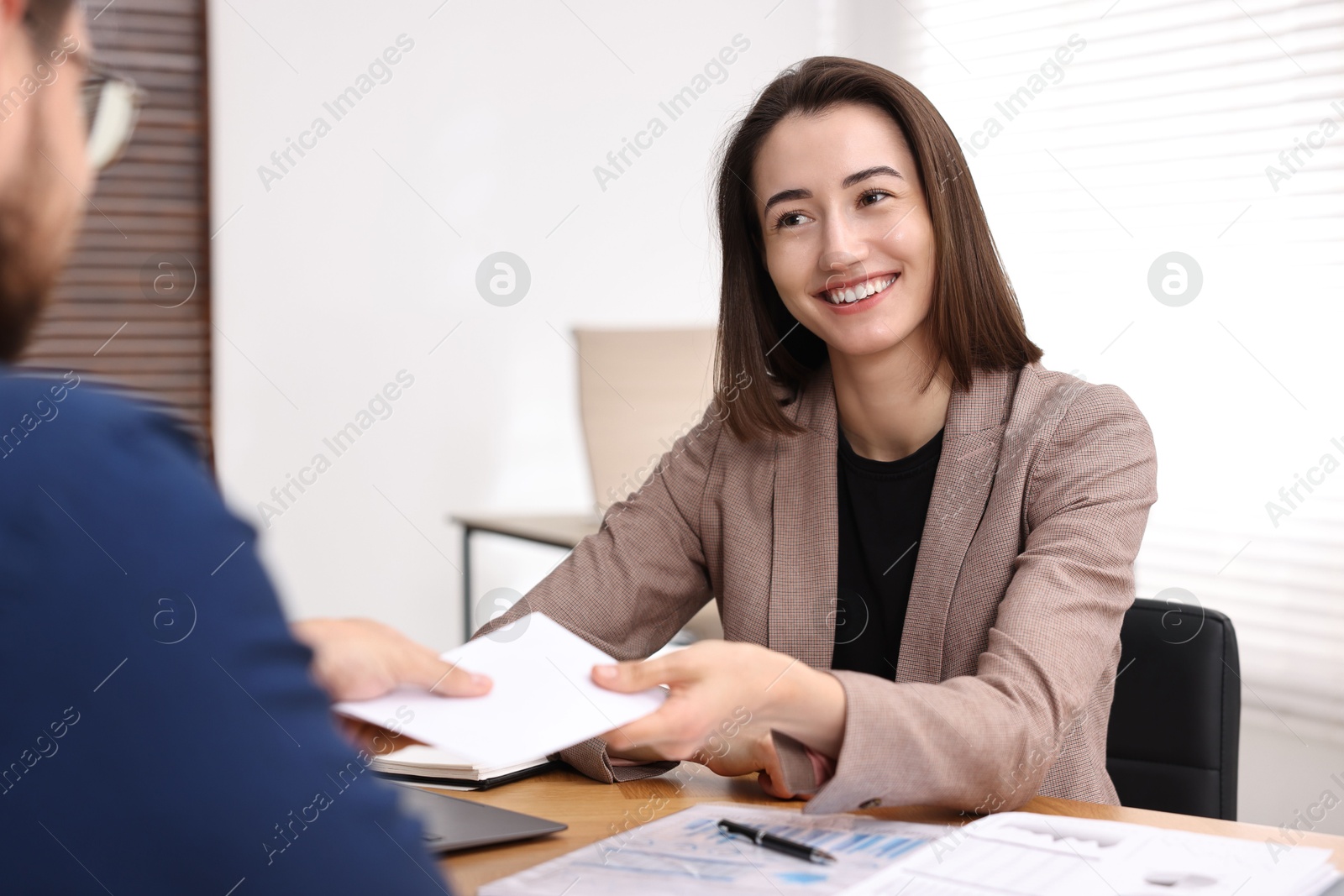 Photo of Boss giving salary in paper envelope to employee indoors