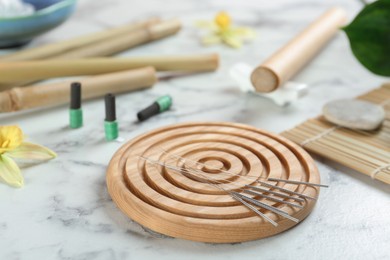 Wooden coaster with acupuncture needles on white marble table