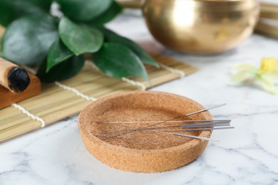 Photo of Cork plate with acupuncture needles on white marble table