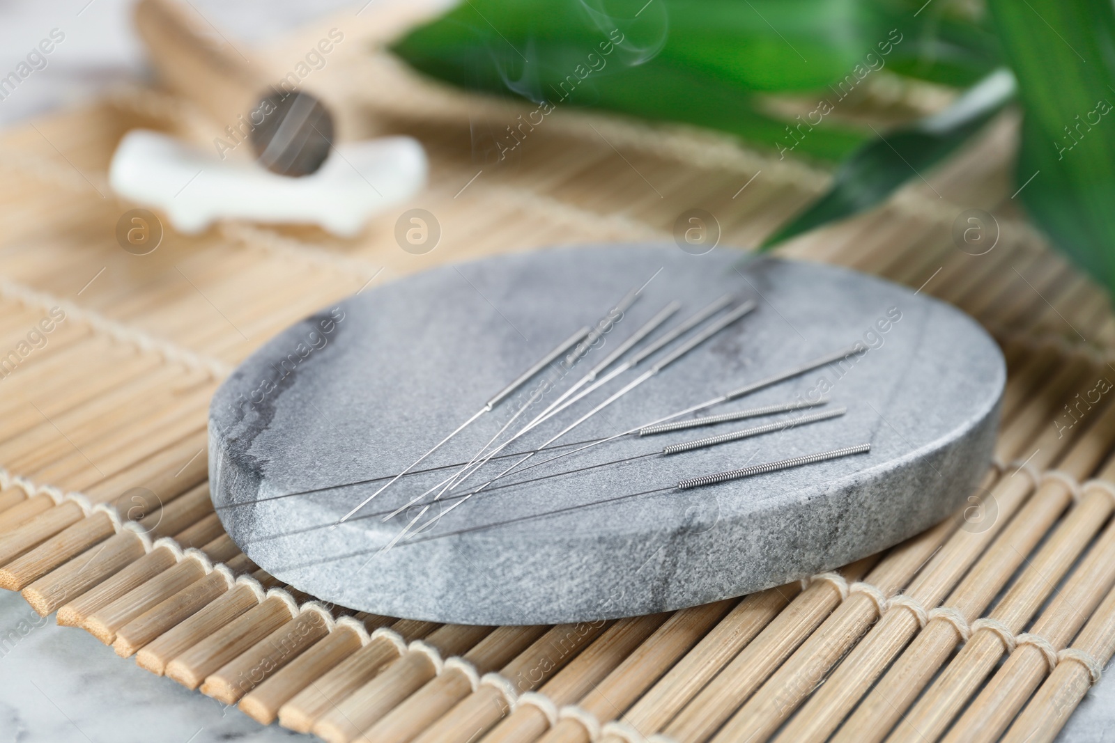 Photo of Grey stone coaster with acupuncture needles on bamboo mat, closeup