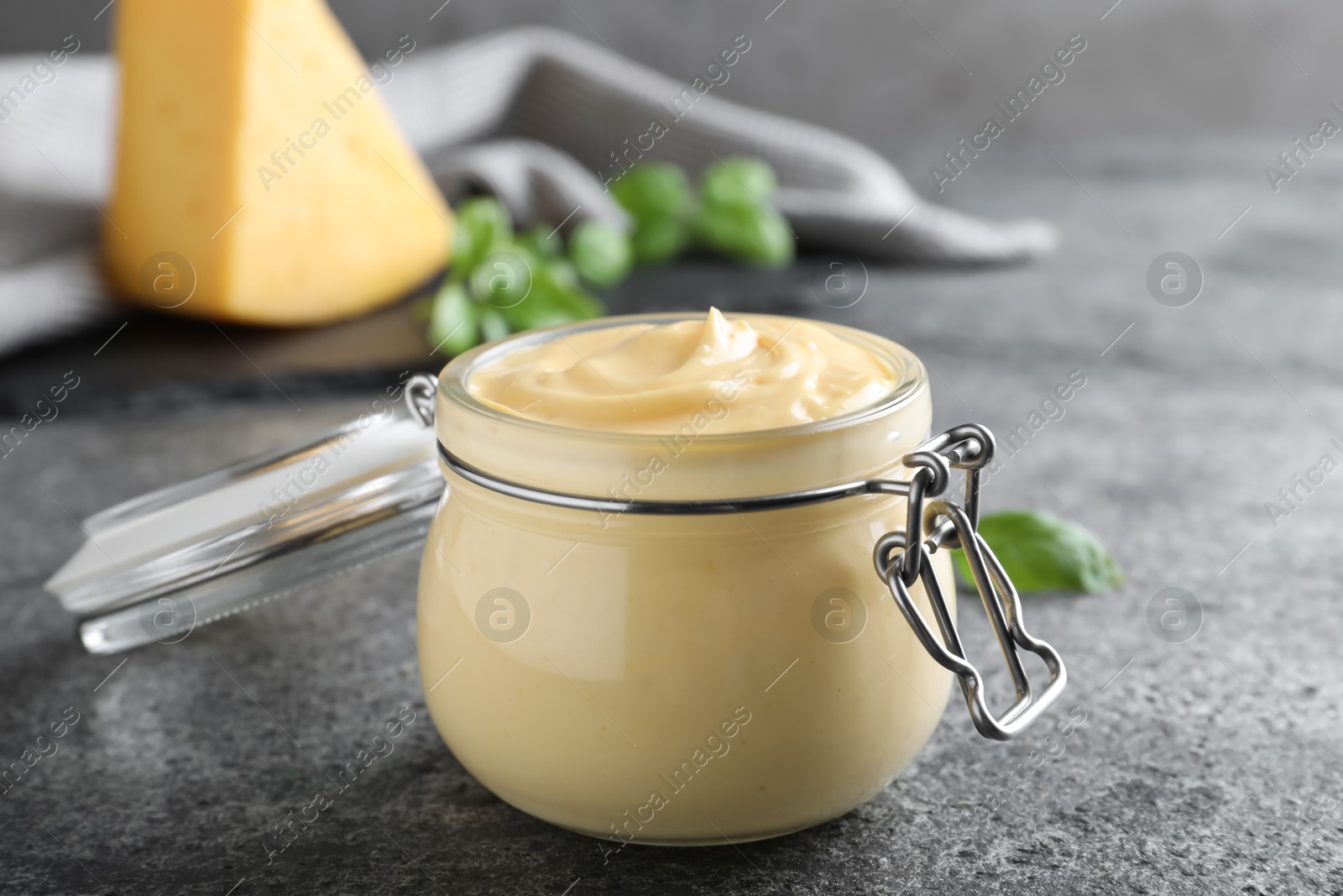 Photo of Tasty cheese sauce in glass jar on grey table, closeup