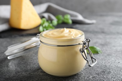 Photo of Tasty cheese sauce in glass jar on grey table, closeup