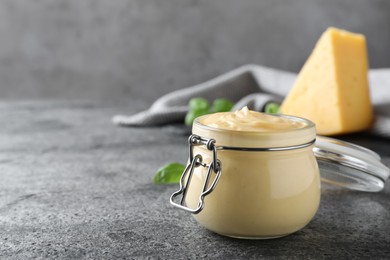 Photo of Tasty cheese sauce in glass jar on grey table, space for text