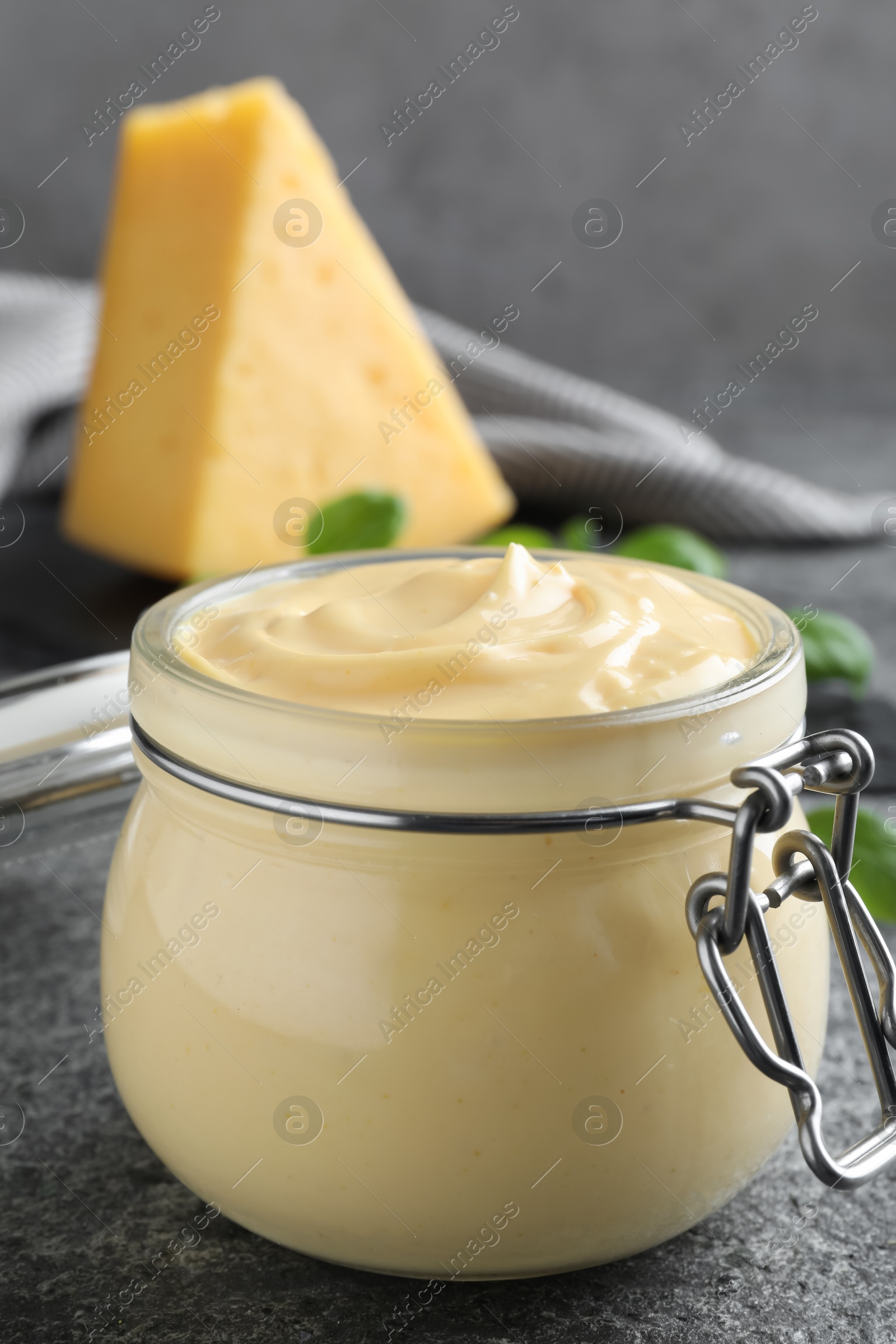 Photo of Tasty cheese sauce in glass jar on grey table, closeup