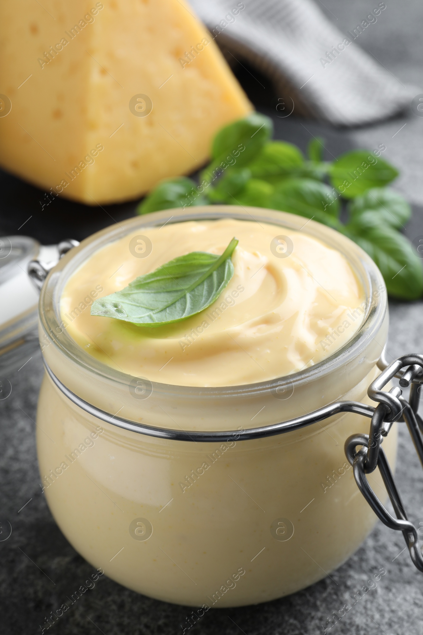 Photo of Tasty cheese sauce with basil in glass jar on grey table, closeup