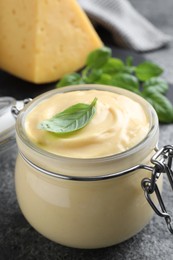 Tasty cheese sauce with basil in glass jar on grey table, closeup