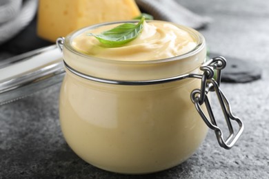 Photo of Tasty cheese sauce with basil in glass jar on grey table, closeup